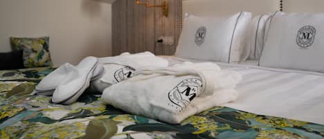 A neatly made bed with a floral bedspread, white pillows with a logo, and a pair of slippers on the bed.