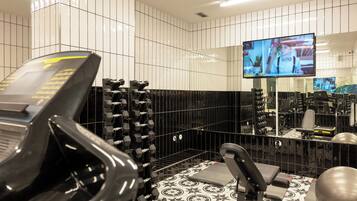 Un gimnasio con equipo de ejercicio, televisión y pared de azulejos.