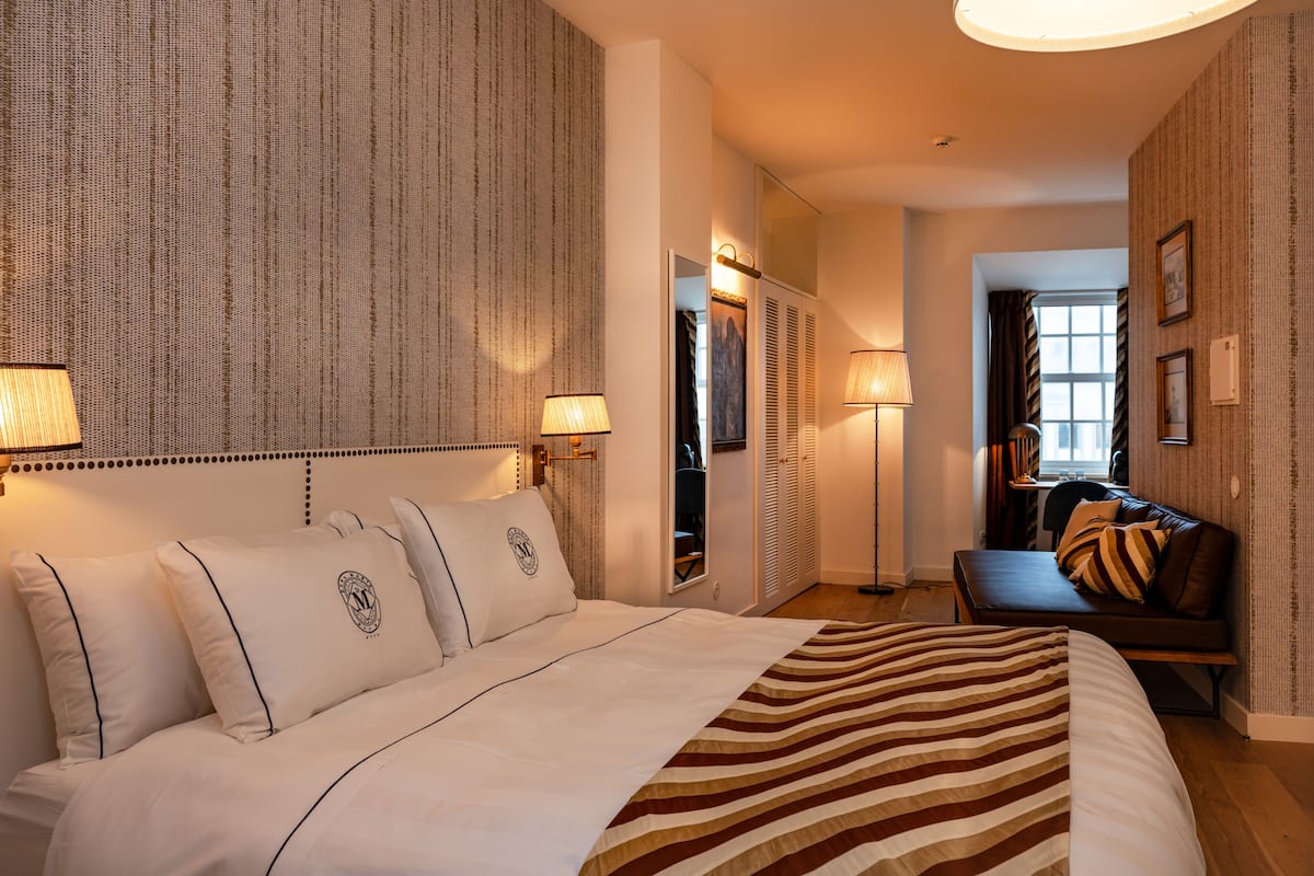 Ein Hotelzimmer mit einem großen Bett, Nachttischlampen, einem Sofa und einem Spiegel.