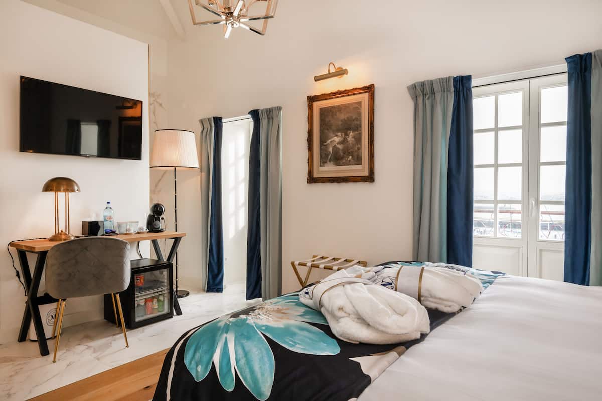 Ein Hotelzimmer mit einem Bett, einem Schreibtisch mit Stuhl, einem Fernseher, einem Bild an der Wand und einem Fenster mit Vorhängen.