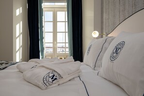 Quarto de hotel com cama bem arrumada, janela com cortinas e luminária na mesinha de cabeceira.