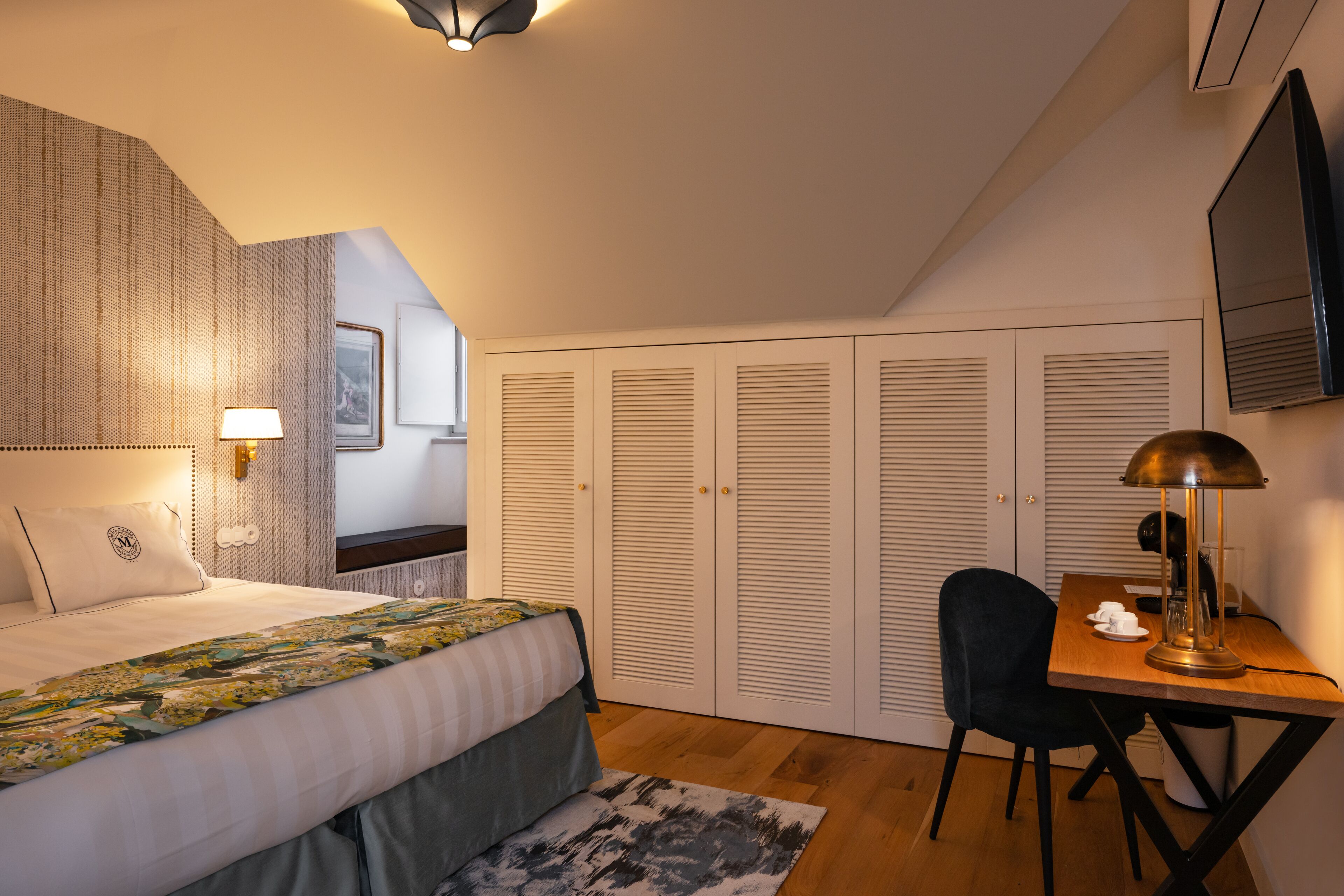 A bedroom with a bed, bedside table, lamp, chair, desk, and a wardrobe.