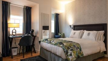 Een moderne hotelkamer met een bed, bureau, stoel en een groot raam met gordijnen.