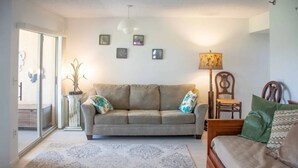 A living room with a sofa, a wooden bed, a lamp, and a wall with framed pictures. - Jupiter Bay Beach Condo (Jupiter)