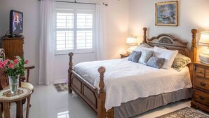 A neatly arranged bedroom with a wooden bed, bedside lamps, a television, and a painting on the wall. - Jupiter Bay Beach Condo (Jupiter)