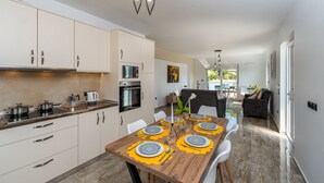 A modern kitchen with white cabinets, a wooden dining table set with yellow placemats, and a view of the outdoor patio. - Sweet Home Apartments (Rhodes)