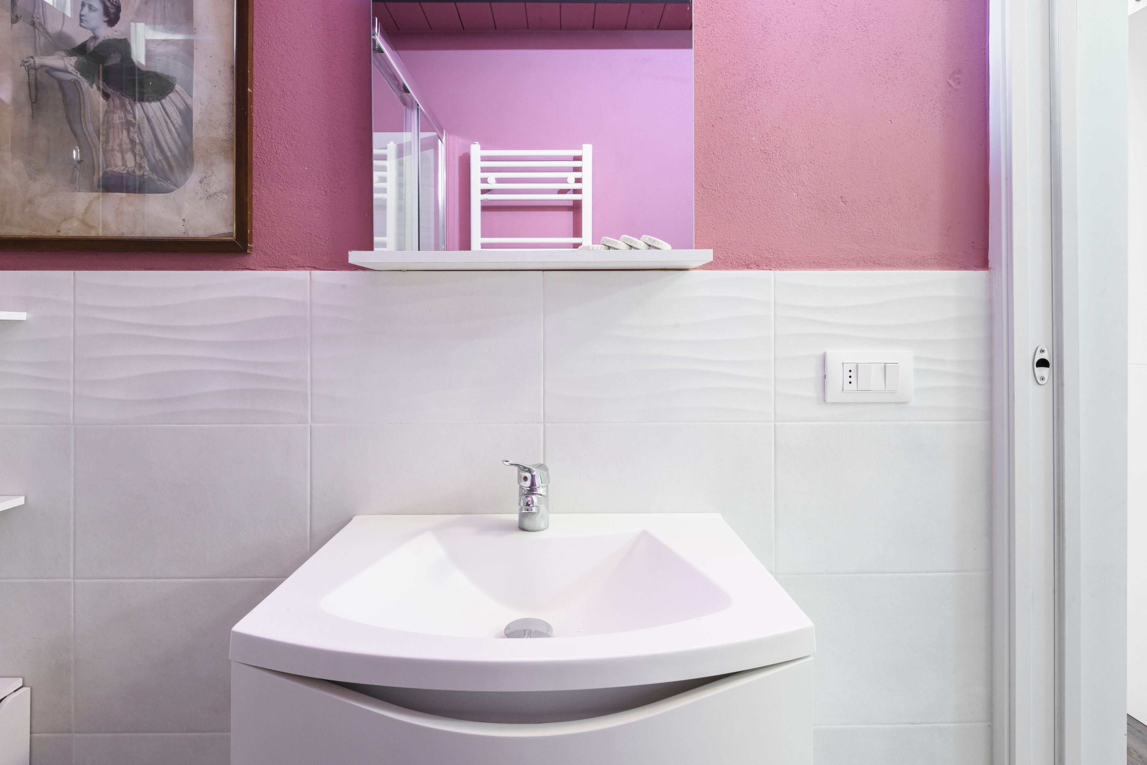 A bathroom with a white sink, a mirror, and a pink wall.