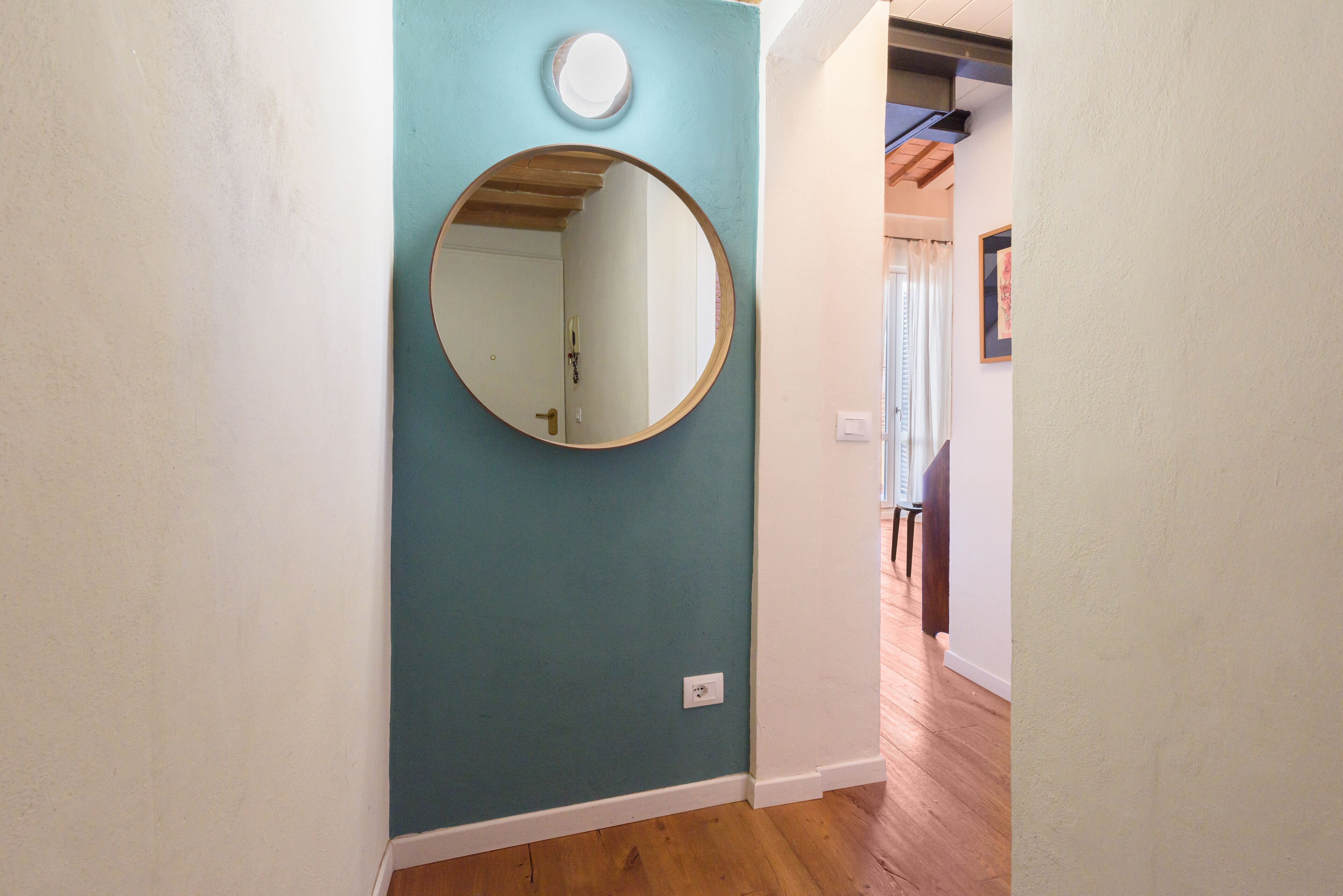 A hallway with a teal wall, a round mirror, and wooden flooring.