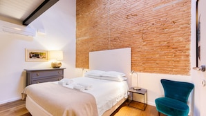 A bedroom with a brick wall, a bed with white linens, a teal chair, a small bedside table with a lamp, and a framed picture on the wall. - Terrace on the roof by Mmega (Florence)
