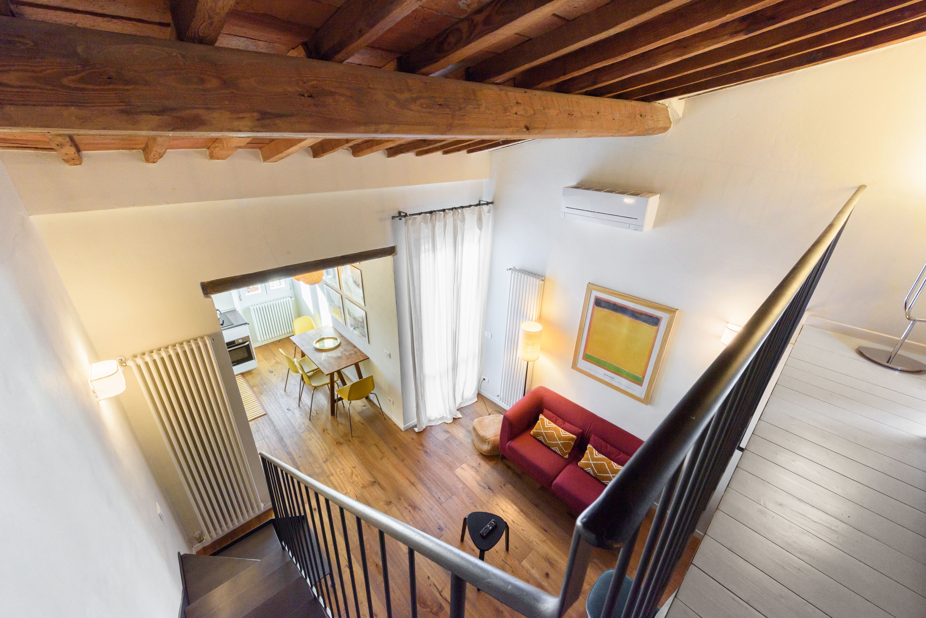 A spacious living area with a wooden ceiling, a red sofa, and a dining area with yellow chairs.
