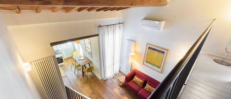 A spacious living area with a wooden ceiling, a red sofa, and a dining area with yellow chairs.