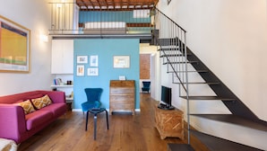 A spacious living area with a wooden floor, a red sofa, a blue chair, a wooden chest of drawers, and a black spiral staircase. - Terrace on the roof by Mmega (Florence)