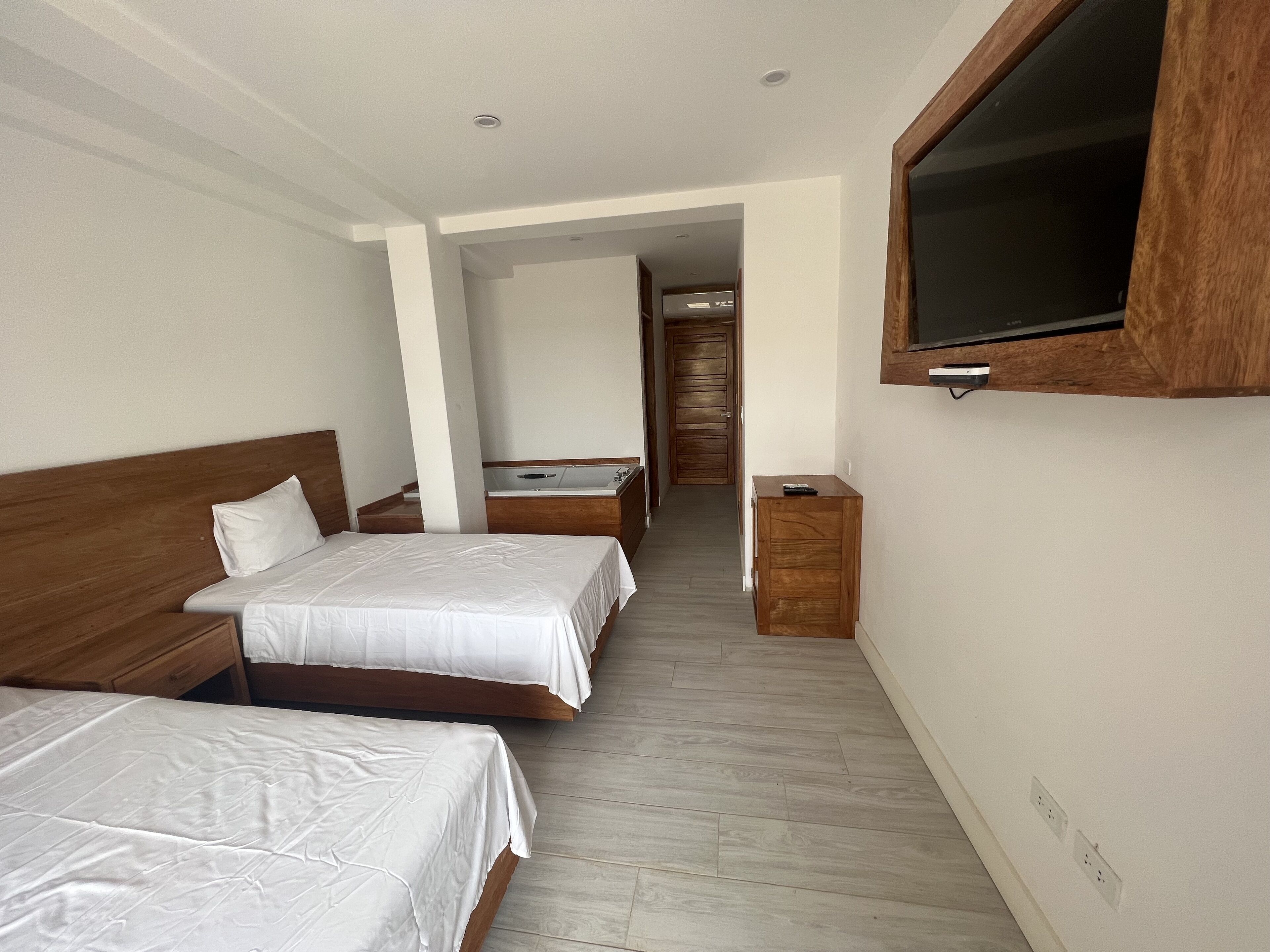 A hotel room with two beds, a wooden headboard, a TV mounted on the wall, and a wooden cabinet.
