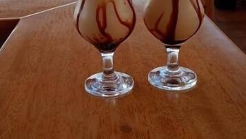 Two tall glasses of a layered beverage on a wooden table at a seaside restaurant with a view of the ocean.