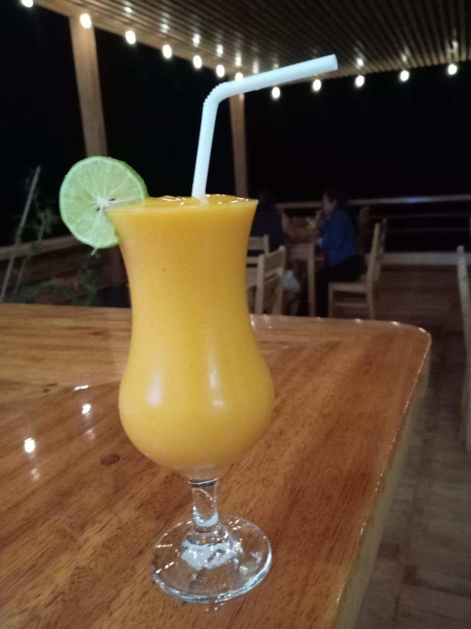 Un cóctel en un vaso con una cuña de lima y una pajita sobre una mesa de madera.
