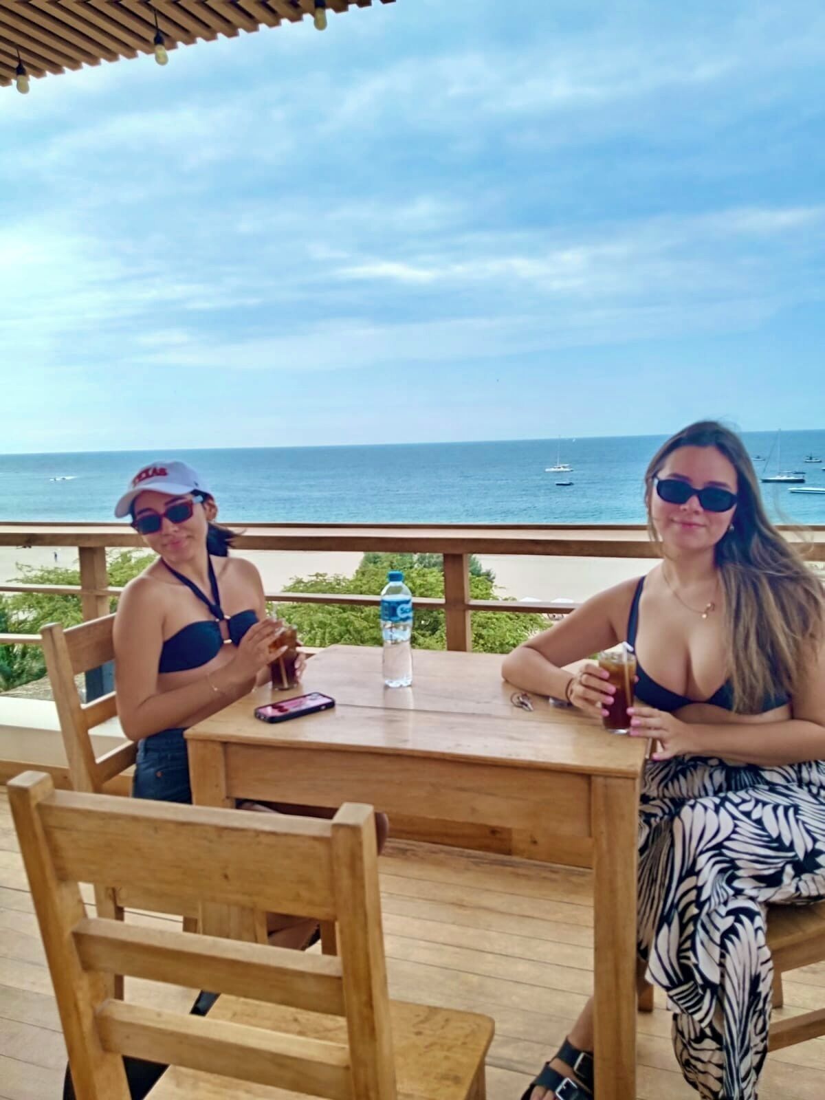 Dos personas sentadas en una mesa de madera con vista al océano y barcos al fondo.