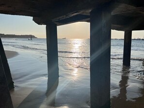 A beach under a pier with clear water and a sunset.