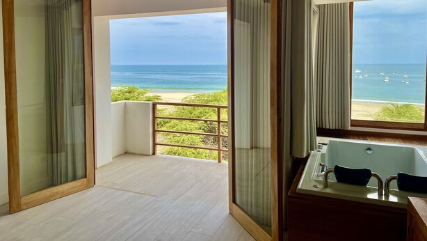 A modern bathroom with a bathtub, a shower, and a large window offering a view of the beach and ocean. - Punta Veleros Rooftop (Los Organos)
