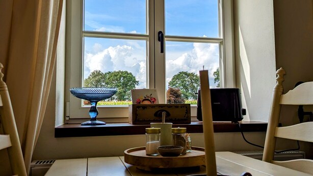 Een kamer met een groot raam, een tafel met kruiden en sausjes, een lamp en een stoel.