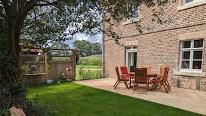 Een bakstenen huis met een terras en een houten tafel en stoelen.
