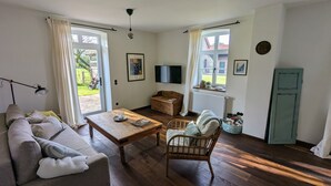 Een gezellige woonkamer met een bank, een houten salontafel, een rieten fauteuil en een televisie op een dressoir.