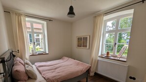 Een slaapkamer met een bed, een radiator, een raam met gordijnen en een zichtbare radiator.