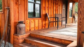A wooden cabin with a porch, steps, a chair, and a window.