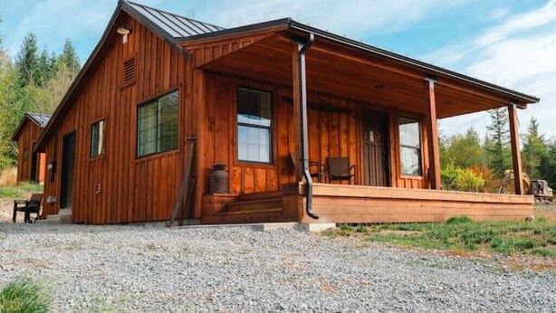 A wooden cabin with a porch, large windows, and a gravel driveway.