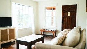 A living room with a sofa, a coffee table, a TV on a cabinet, and a wooden door.