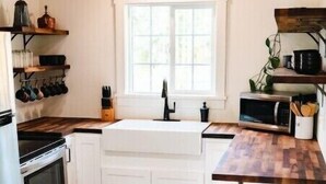 A compact kitchen with white cabinets, a wooden countertop, a stainless steel stove, a sink, and a trash can.