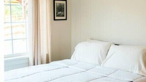 A neatly made bed with white bedding in a room with a window and a picture on the wall.
