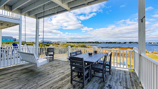 A wooden deck with a table and chairs, overlooking a body of water and a distant shoreline. - Tides and Sunshine - Ocean Views w/ Private Pools! (North Topsail Beach)