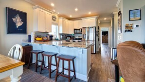 A spacious kitchen with white cabinets, a large island with stools, and modern appliances. - Tides and Sunshine - Ocean Views w/ Private Pools! (North Topsail Beach)