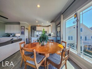 A modern kitchen with white cabinets, a central island, and a dining area with a wooden table and chairs. - Good Day Sunshine: Pool +Dock +Ocean Views! (North Topsail Beach)