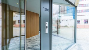 Una entrada de edificio moderna con puerta de vidrio, pared de paneles de madera y cerradura electrónica.