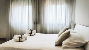 Ein Hotelzimmer mit einem großen Bett, weißen Laken und Blick durch leichte Vorhänge.