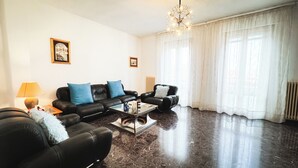 Ein Wohnzimmer mit schwarzer Ledersofa-Garnitur, einem Couchtisch, einer Lampe und einem Kronleuchter.