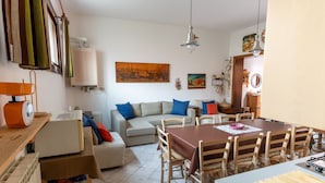 A living room with a sofa, a dining table with chairs, and a kitchen area with a stove. - Casa Aprilia by Ca-Sa Check (Venezia)