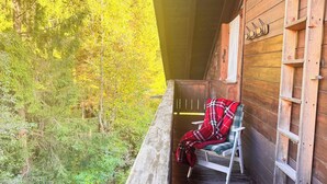 Une cabane en bois avec un banc et une couverture à carreaux, d’où l’on a vue sur une forêt.