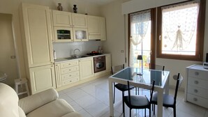 A modern kitchen with white cabinets, a dining table with chairs, and a window with curtains.