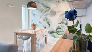 A dining area with a wooden table, white chairs, and a blue rose in a glass vase. - Farmont Seafront Acquamarine Suite by CaSa Check (Chioggia)