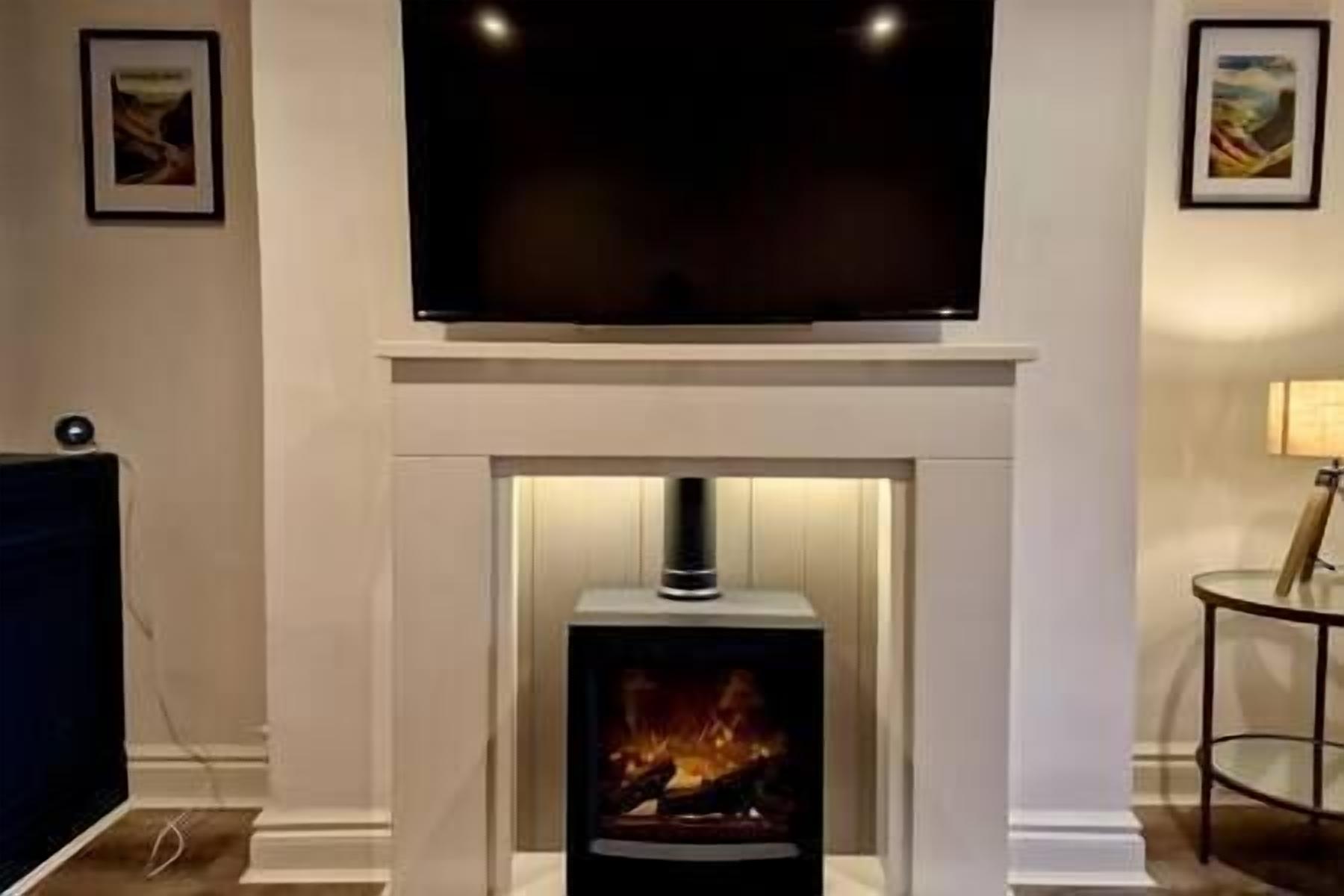 A living room with a fireplace, a flat-screen TV mounted above it, and framed artwork on the walls.