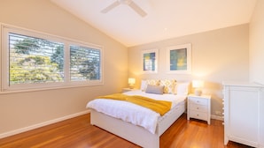 A bedroom with a bed, two bedside tables, a ceiling fan, and two windows with blinds. - Pet friendly La Costa, 2-1a Messines St - air con and Wi-Fi (Shoal Bay)