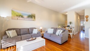 A modern living room with two grey sofas, a white coffee table, and a painting of a beach scene. - Pet friendly La Costa, 2-1a Messines St - air con and Wi-Fi (Shoal Bay)