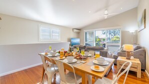 A dining area with a wooden table set for a meal, surrounded by white chairs. - Pet friendly La Costa, 2-1a Messines St - air con and Wi-Fi (Shoal Bay)