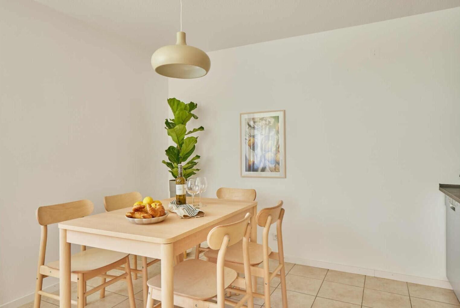 Ein Essbereich mit einem Holztisch, sechs Stühlen, einer Hängeleuchte, einem Blumentopf und einem gerahmten Kunstwerk an der Wand.