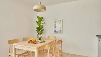 Ein Essbereich mit einem Holztisch, sechs Stühlen, einer Hängeleuchte, einem Blumentopf und einem gerahmten Kunstwerk an der Wand.
