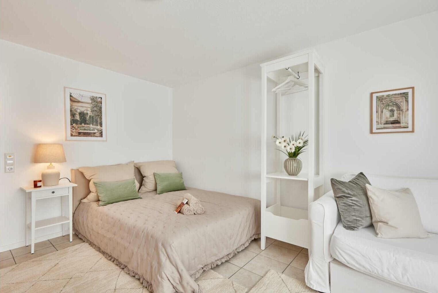 A bedroom with a bed, bedside table, lamp, and a white wardrobe with a shelf.