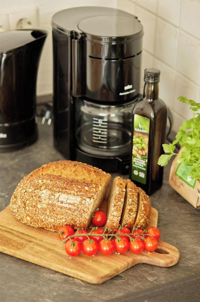 Una pagnotta di pane a fette su un tagliere di legno, una bottiglia d'olio d'oliva e pomodorini ciliegino su un piano di lavoro della cucina.