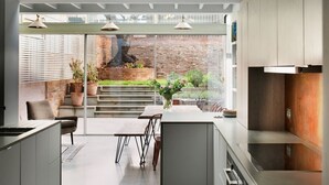 A modern kitchen with a central island, built-in appliances, and a view of a brick wall and garden. - Sublime 4BD House W/park Views - London Fields! (London)